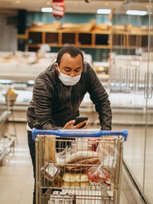 Man wearing mask shops in a supermarket, pushing a cart in the aisle.